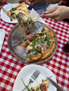 A savory pizza being served on a checkered tablecloth outdoors.