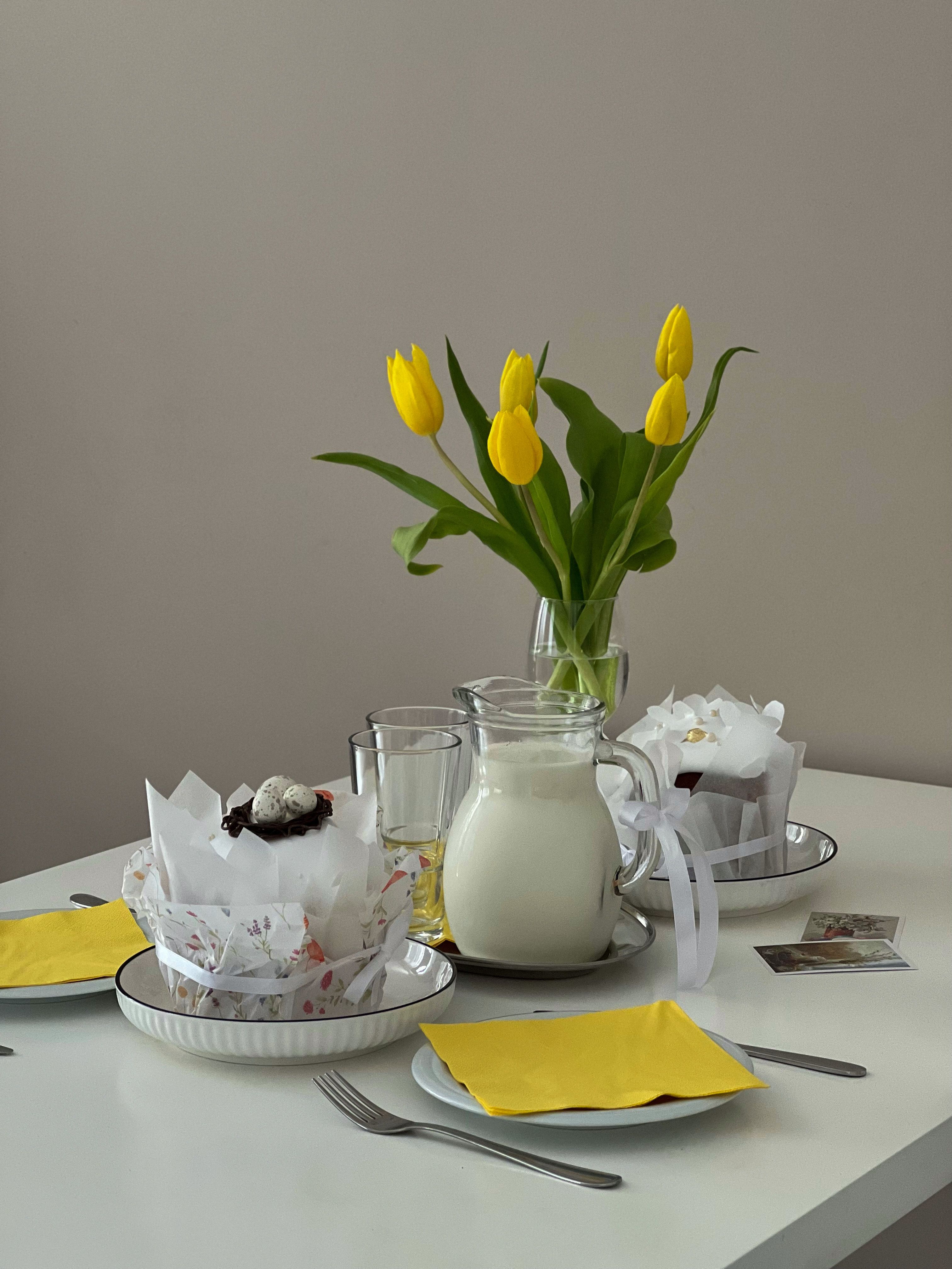 Charming breakfast setup with yellow tulips, milk jug, and pastries, creating a warm and inviting atmosphere.