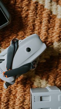 Top view of a compact drone with propellers on a textured patterned rug indoors.