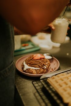 Close-up of a chef preparing desserts, focusing on a chocolate waffle with strawberries in a rustic kitchen setting.