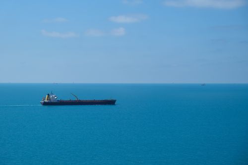 Free A cargo ship sails smoothly across a vast, clear blue ocean under a bright, sunny sky. Stock Photo