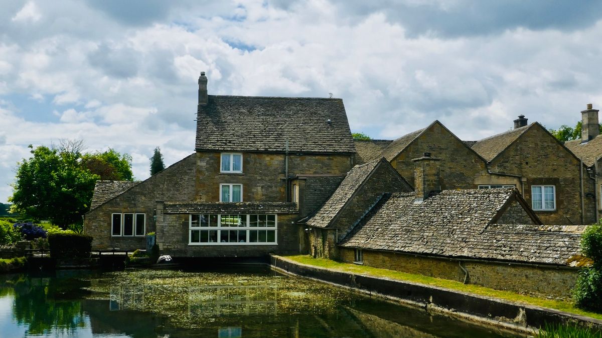 A Cotswold stone mill and houses reflected in a still pond, a calm setting for a group weekend away in the Cotswolds