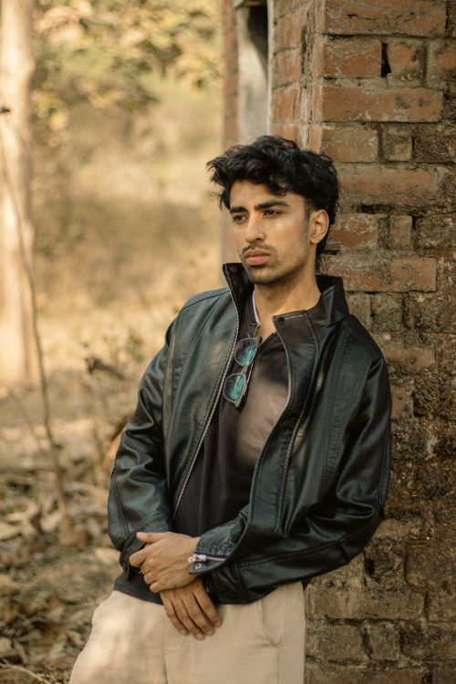 Free Portrait of a man in a black leather jacket standing outdoors against a brick wall. Stock Photo