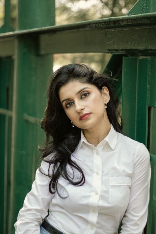 Free A woman in a white shirt leans against a green metal structure outdoors, exuding a serene and thoughtful expression. Stock Photo