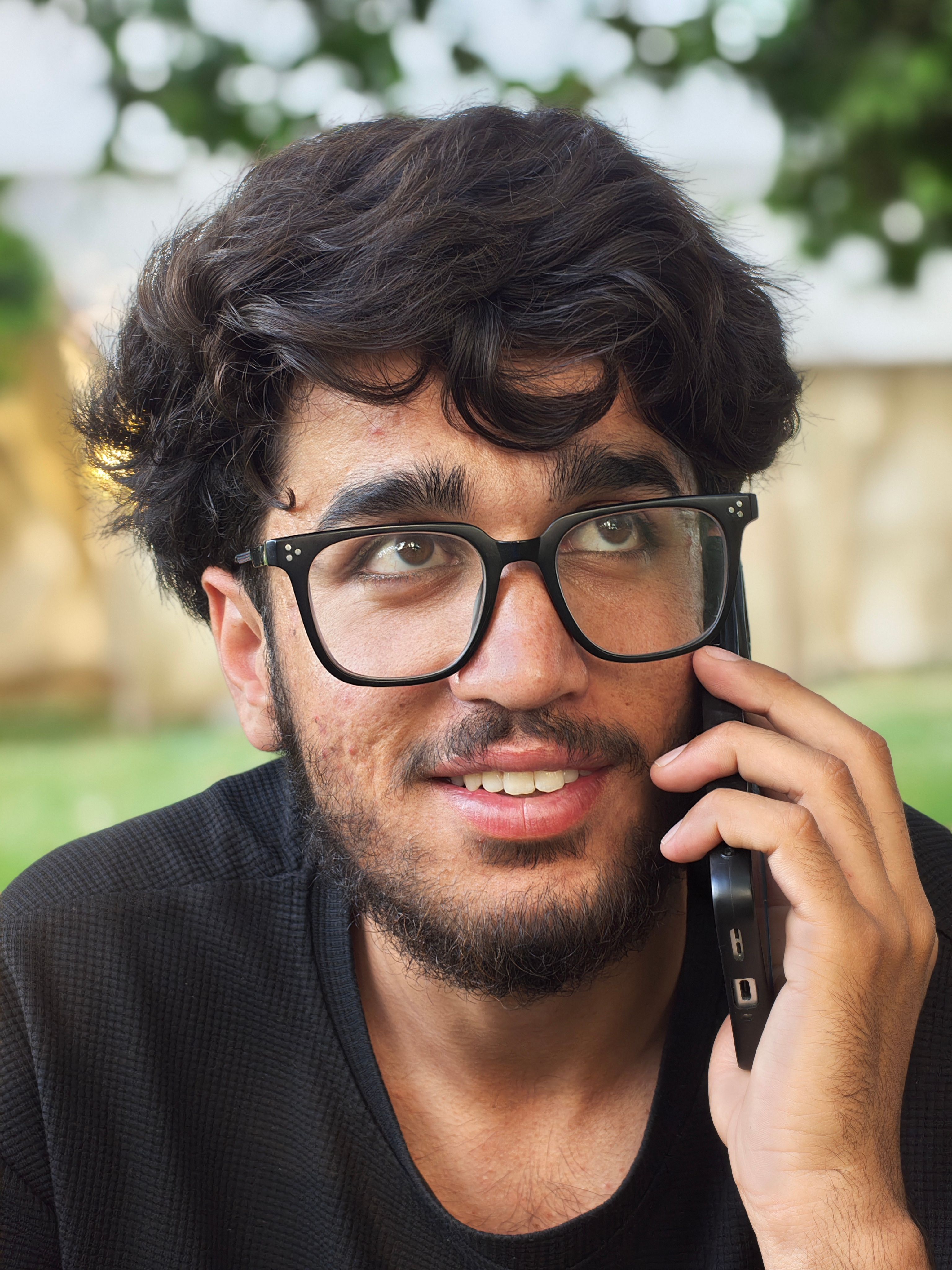 A young man with glasses uses his phone outdoors, conveying a casual lifestyle.