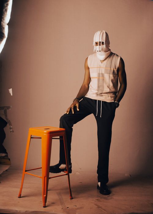 Free Artistic portrait of a masked model standing with an orange stool highlighting a unique fashion style. Stock Photo