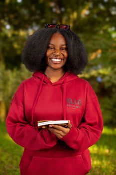 Happy woman wearing red hoodie holding a book outside in a park.