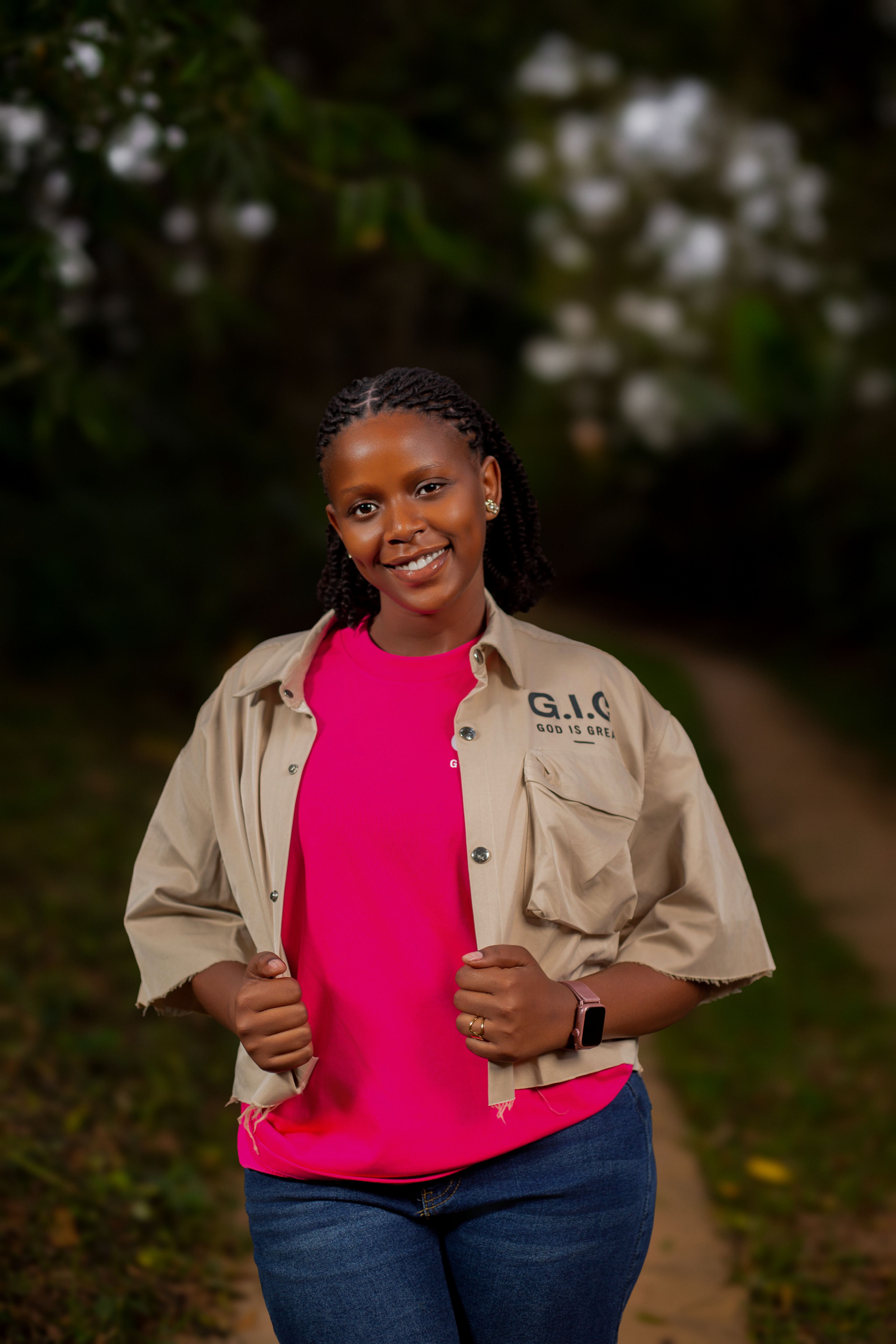 A young woman smiles warmly while posing outdoors on a tranquil path.