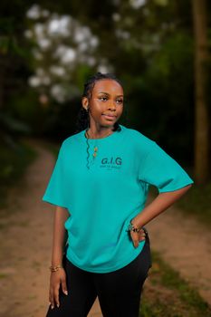 Confident young woman posing outdoors in a green shirt on a wooded path.