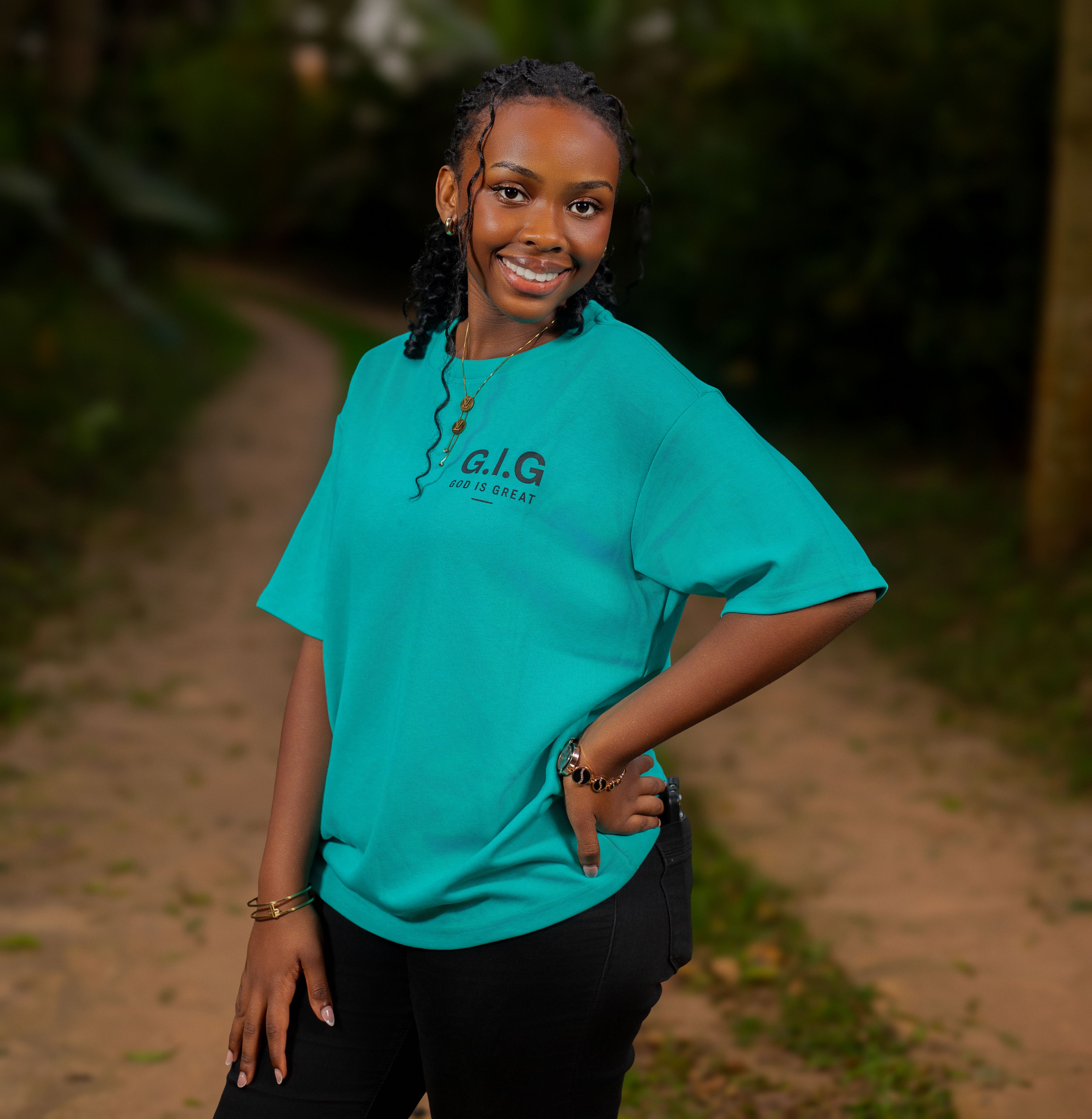A young woman smiling confidently in a teal t-shirt outdoors on a nature path.