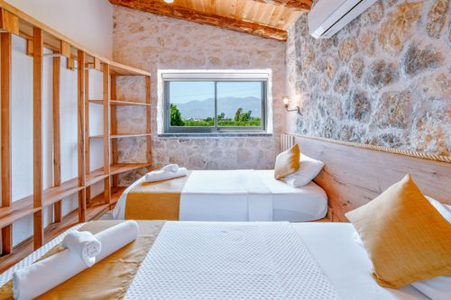 Free Charming bedroom with stone walls and twin beds overlooking serene mountains through a window. Stock Photo