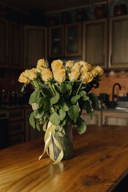 Free A beautiful bouquet of yellow roses in a glass vase, adding charm to a rustic kitchen setting. Stock Photo