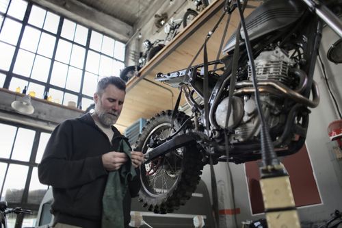 Free An experienced mechanic working on a motorcycle in a well-lit workshop. Industrial setting with focus on repair and maintenance. Stock Photo
