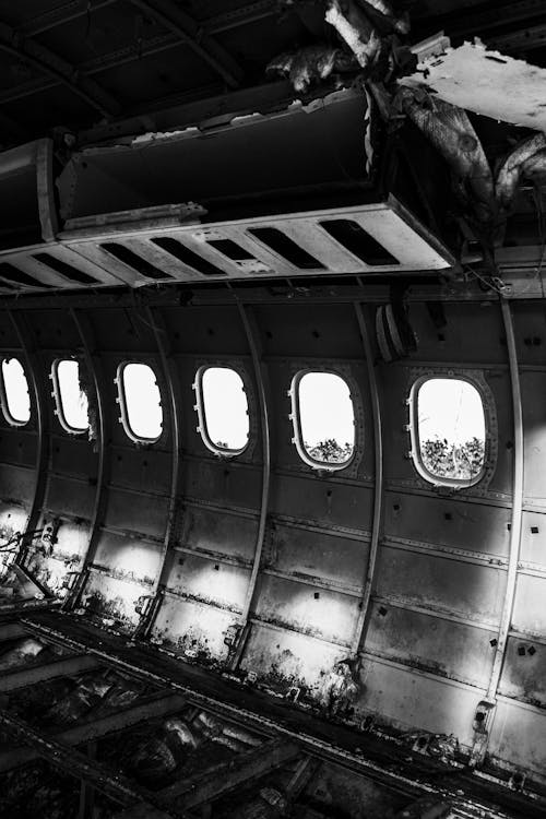 Interior of gray aged plane cabin with similar rounded windows and damaged metal rack and dirty surface after having accident