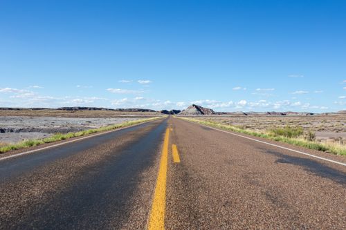 Free A solitary desert highway stretches under a bright blue sky, leading to rugged distant hills. Stock Photo