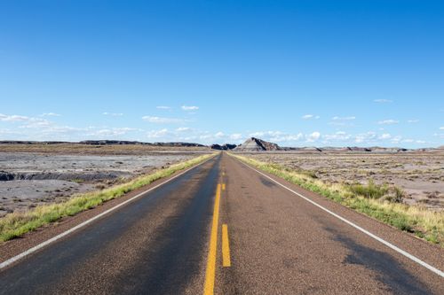 Free A straight road stretches through a desert landscape under a clear blue sky, offering a sense of endless journey. Stock Photo