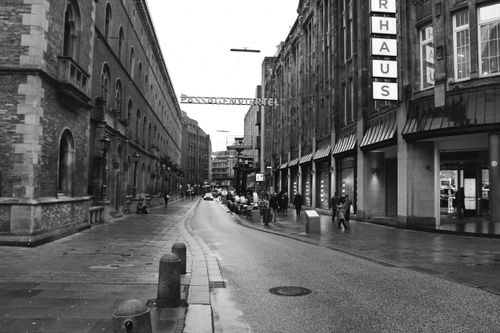 Free A monochromatic city street with buildings and pedestrians, overcast day. Stock Photo
