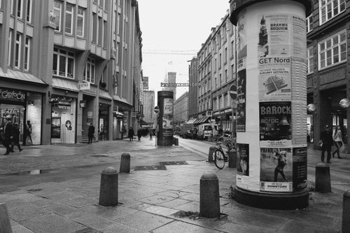 Free Monochrome city street scene featuring posters on columns and pedestrians. Stock Photo