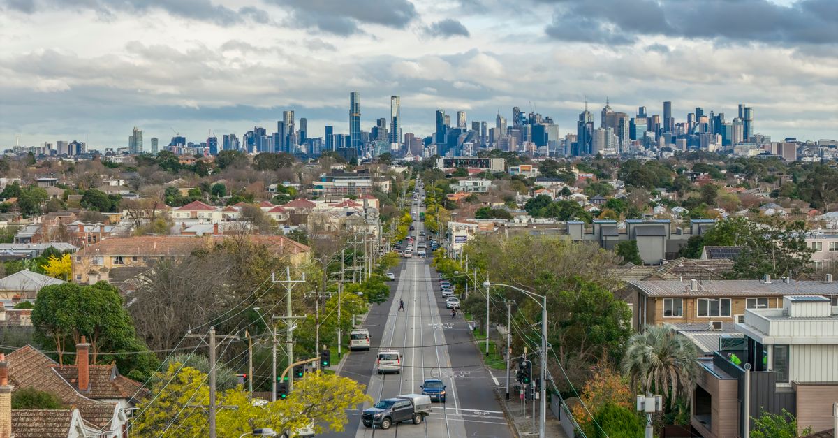 An expansive view of Melbourne's suburban road leading to the city skyline with lush greenery and overcast skies.