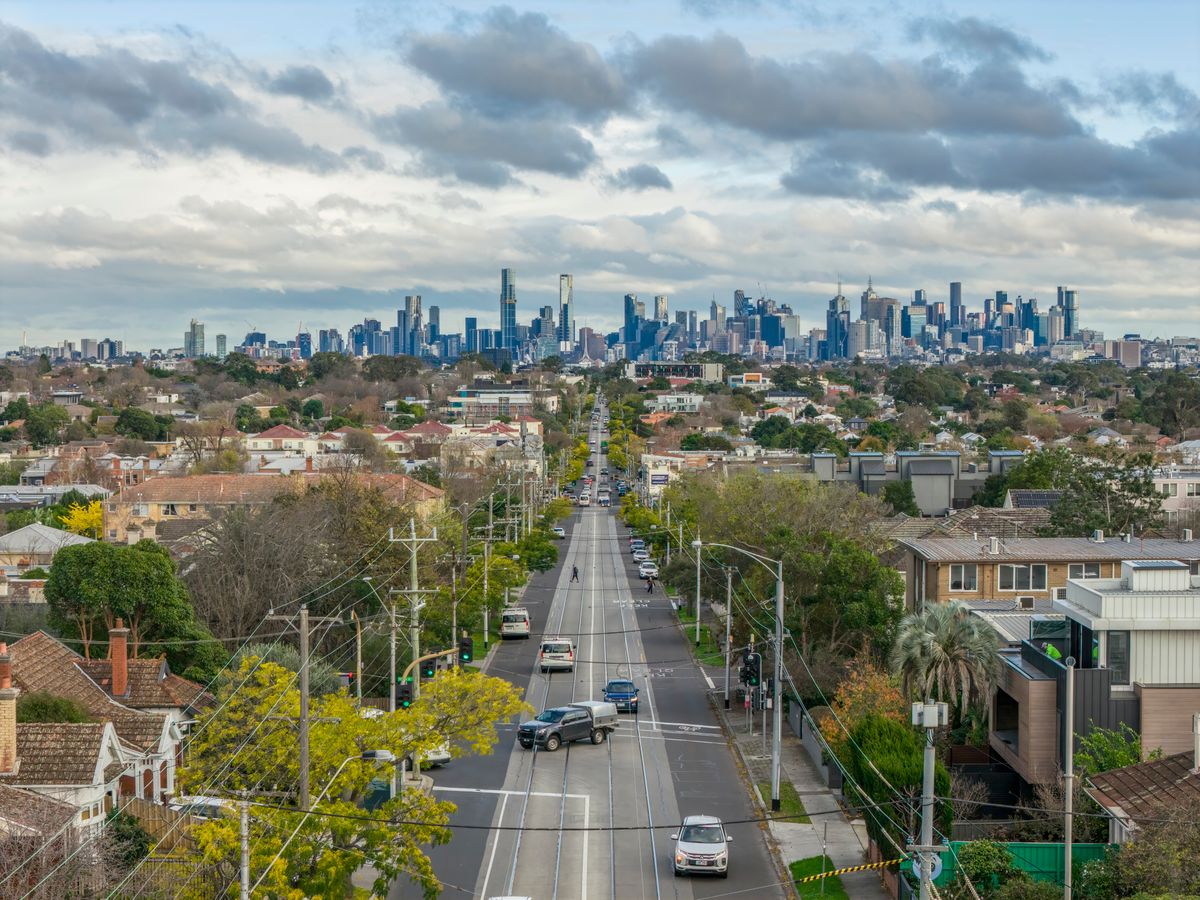 A suburban Australian street running toward a distant city skyline