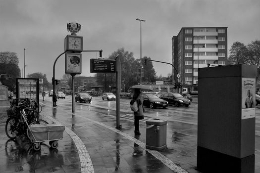 Black and white rainy city scene with people, traffic, and high-rise buildings.