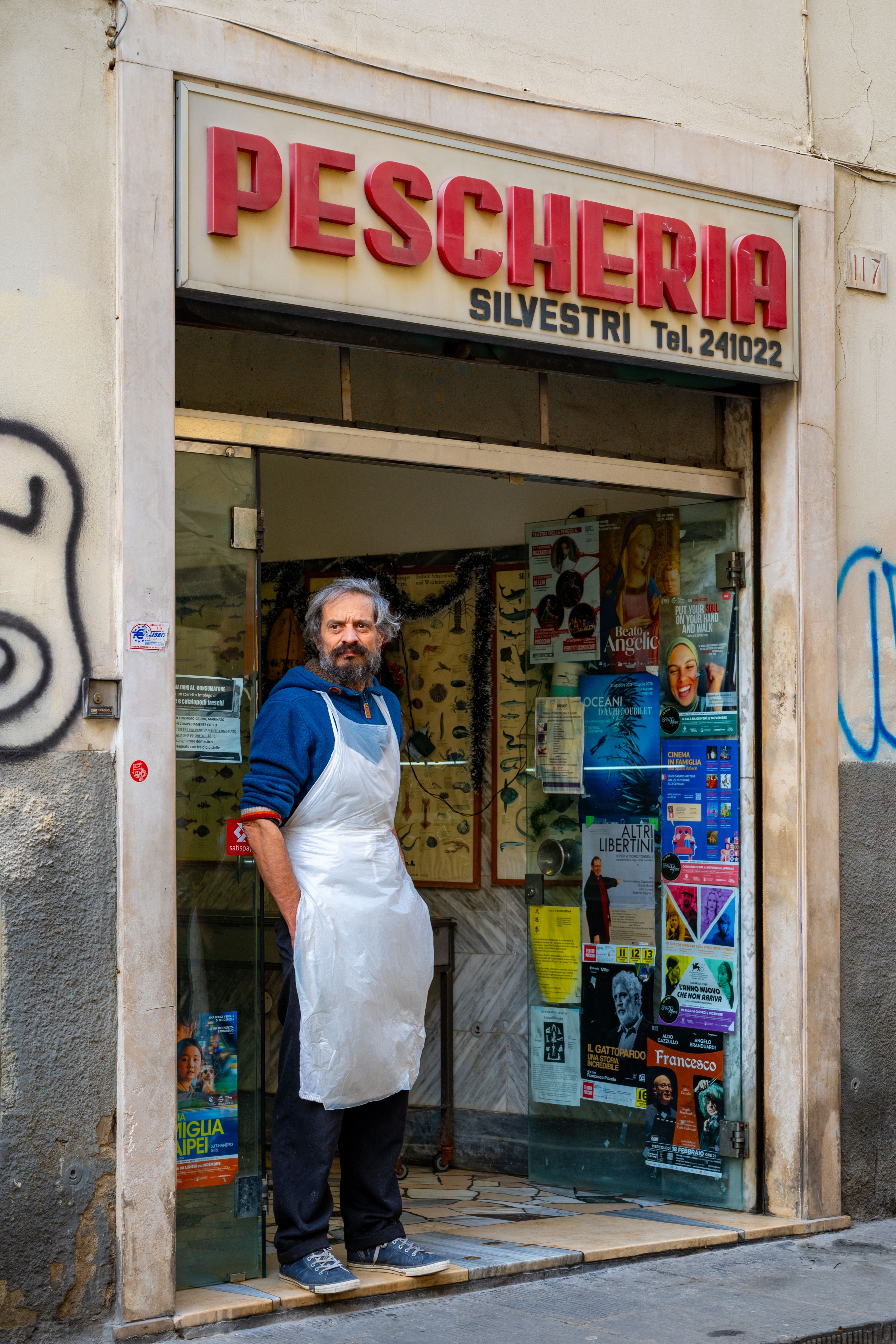 A male fishmonger stands outside his shop, Pescheria Silvestri, smiling.