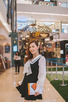 一位优雅的亚洲女子在现代购物中心里拿着平板电脑微笑