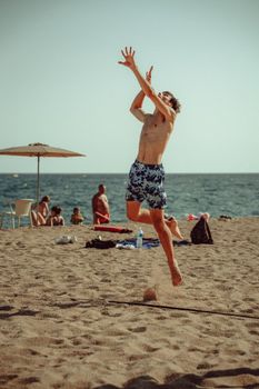 A man in swim shorts jumps on a sunny beach in Lloret de Mar, Spain.