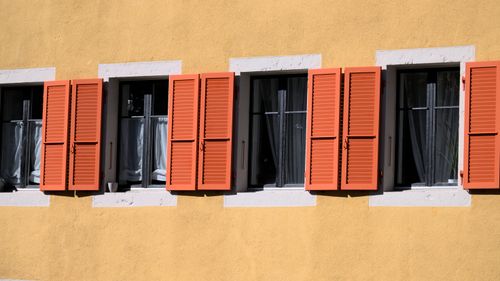 Free A sunny facade with red shutters against a mustard yellow wall, creating a vibrant contrast. Stock Photo