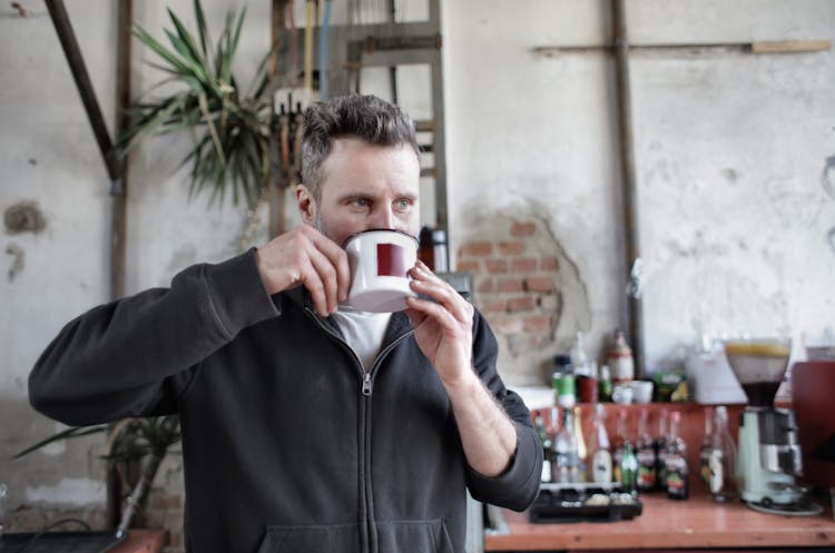 Man In Black Zip Up Jacket Holding White Ceramic Mug