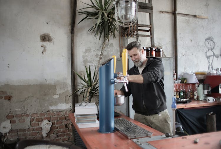 Happy Male Mechanic Pouring Water In Saucepan In Shabby Workshop