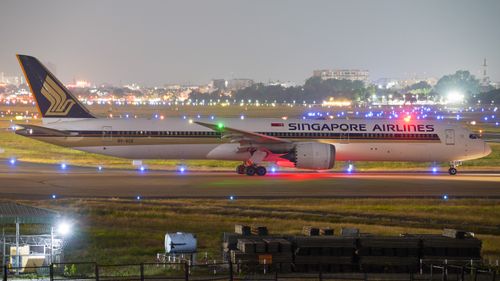 Free A Singapore Airlines Boeing 787 Dreamliner on the runway at night with vibrant city lights in the background. Stock Photo