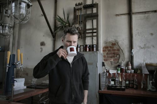 Man in Black Jacket Drinking From White Ceramic Mug