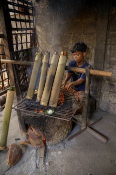 A young person cooking food in bamboo over an open fire, showcasing Balinese culinary tradition.
