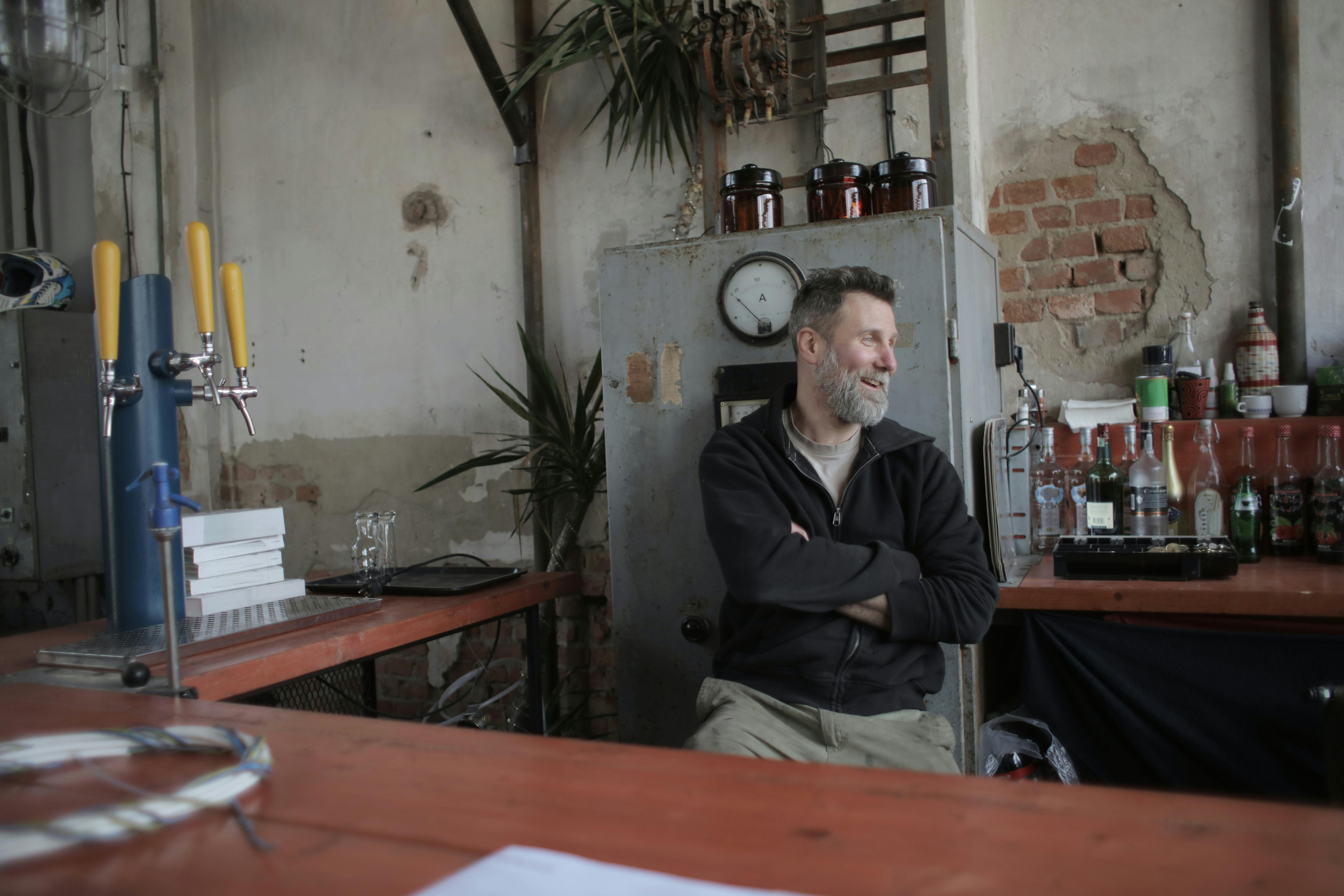 一名男子随意坐在乡村酒吧里，双臂交叉，微笑着说话