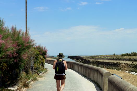 A woman with a backpack walks along a coastal path in sunny Nouvelle-Aquitaine, France.