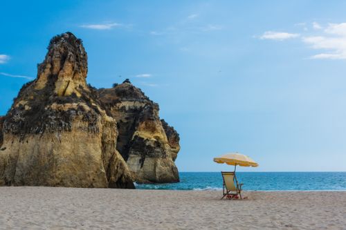 Free A peaceful beach setting with a solitary umbrella and chair by rocky cliffs. Stock Photo