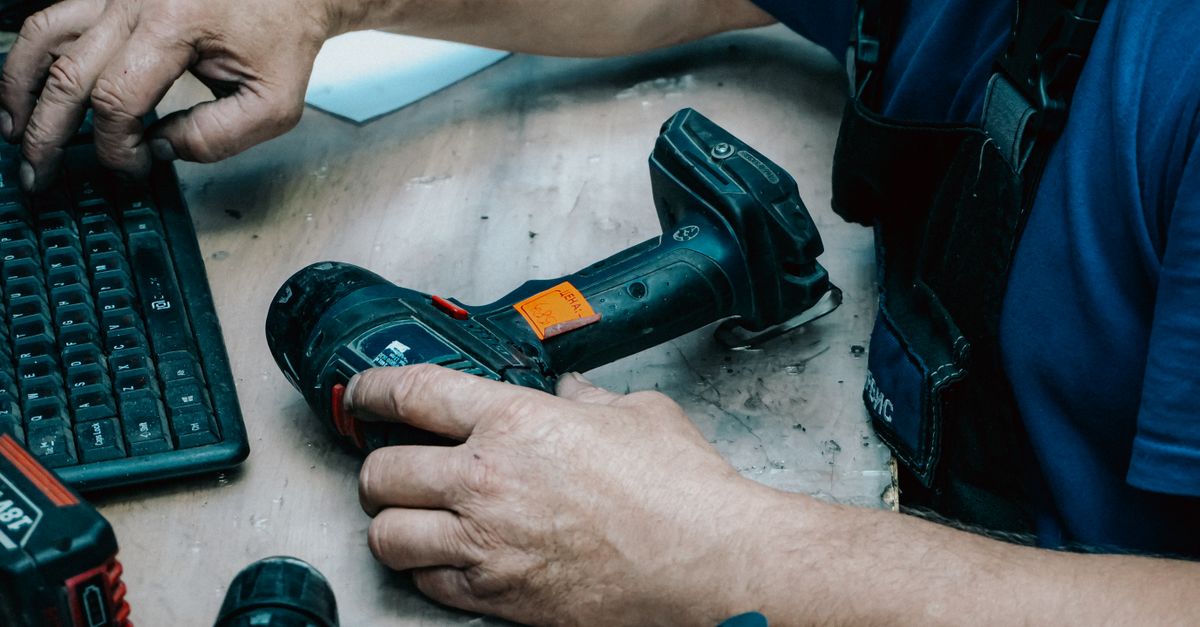 A technician operates a keyboard while holding a cordless drill at a workstation.