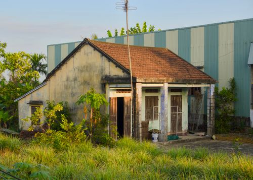 Free A rustic rural house with a tiled roof surrounded by lush greenery under a clear sky. Stock Photo