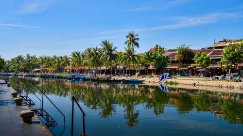 Free Beautiful riverside scene in Hoi An with traditional buildings and palm trees reflecting in the water. Stock Photo
