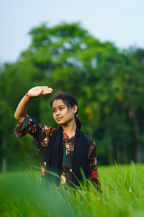 Free A young woman enjoys a sunny day in a lush green field in Rangpur, Bangladesh. Stock Photo