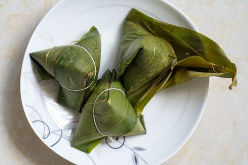 Free Close-up of three traditional leaf-wrapped dumplings on a decorative white plate. Stock Photo