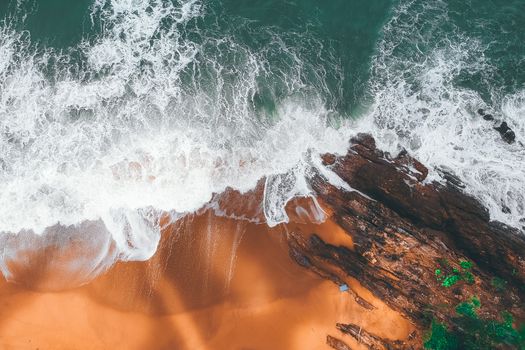 Drone shot capturing ocean waves crashing on rocks and sandy shore in Chukai, Malaysia.