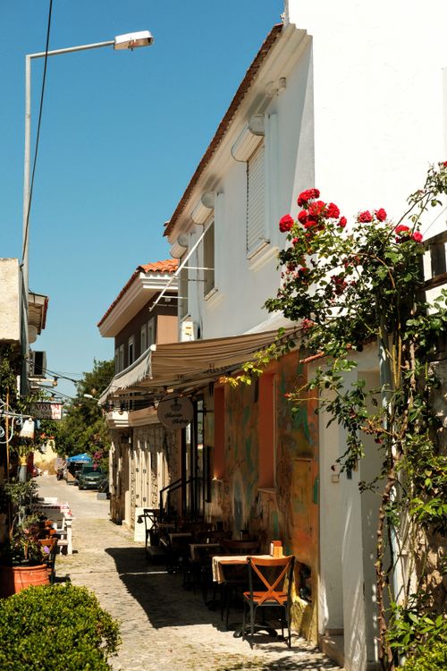 Free Quaint Mediterranean street scene showcasing vibrant facades, a peaceful sidewalk café, and lush floral accents. Stock Photo