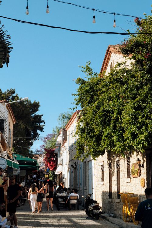 Free Cobblestone street with people dining and exploring in a picturesque, sunny Mediterranean town. Stock Photo
