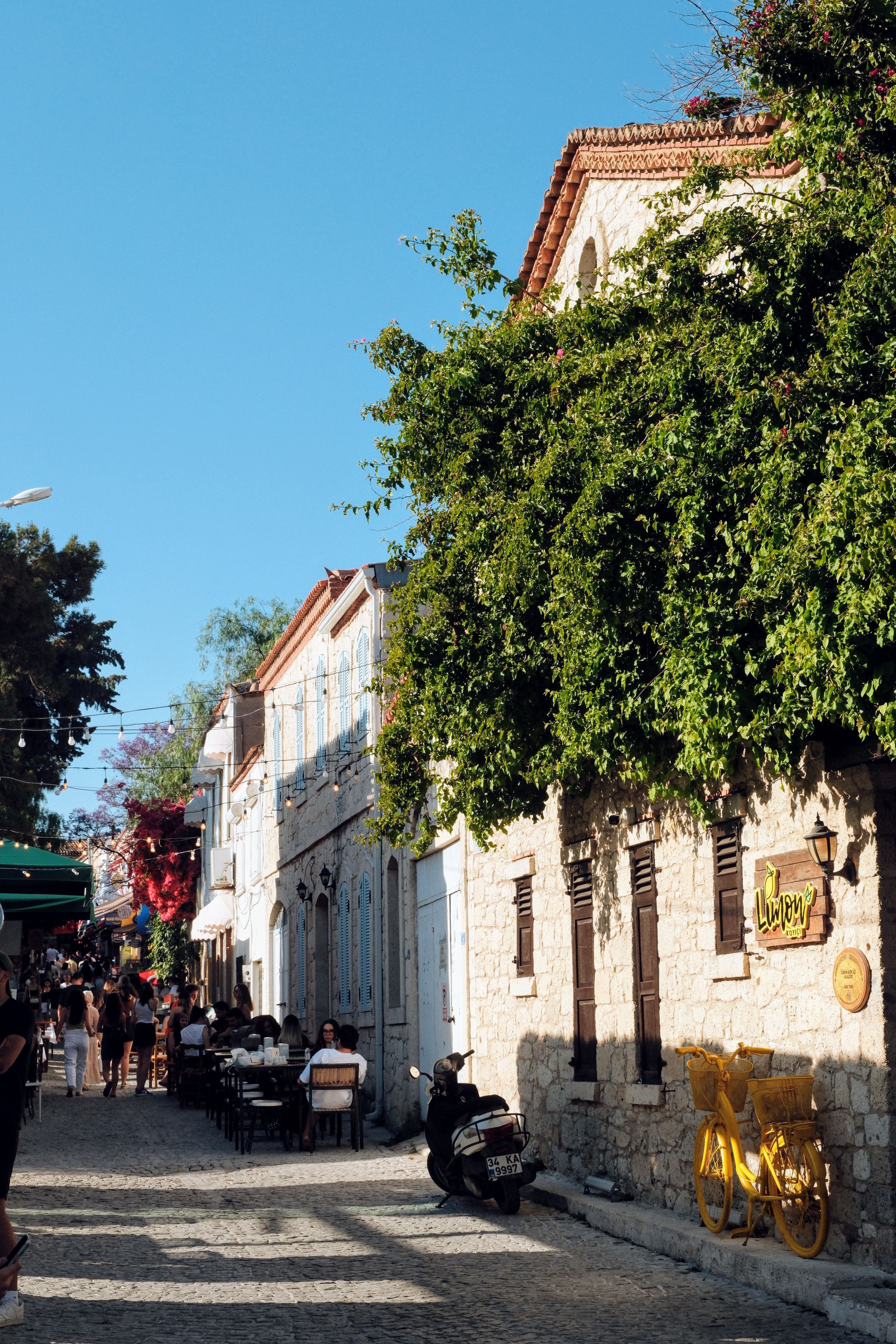 Quaint European street scene with outdoor cafes and a yellow bicycle, under a clear blue sky.