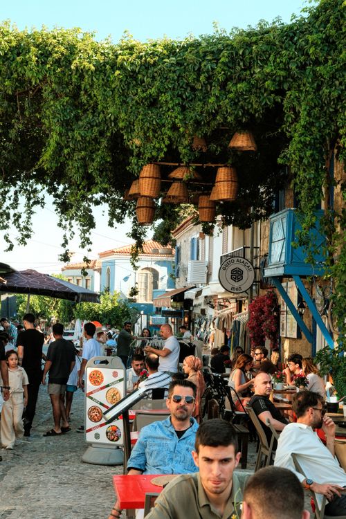 Free People enjoying alfresco dining under lush greenery in a lively street setting on a sunny day. Stock Photo