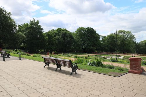 Free Tranquil urban park scene featuring benches, lush greenery, and clear blue sky. Stock Photo
