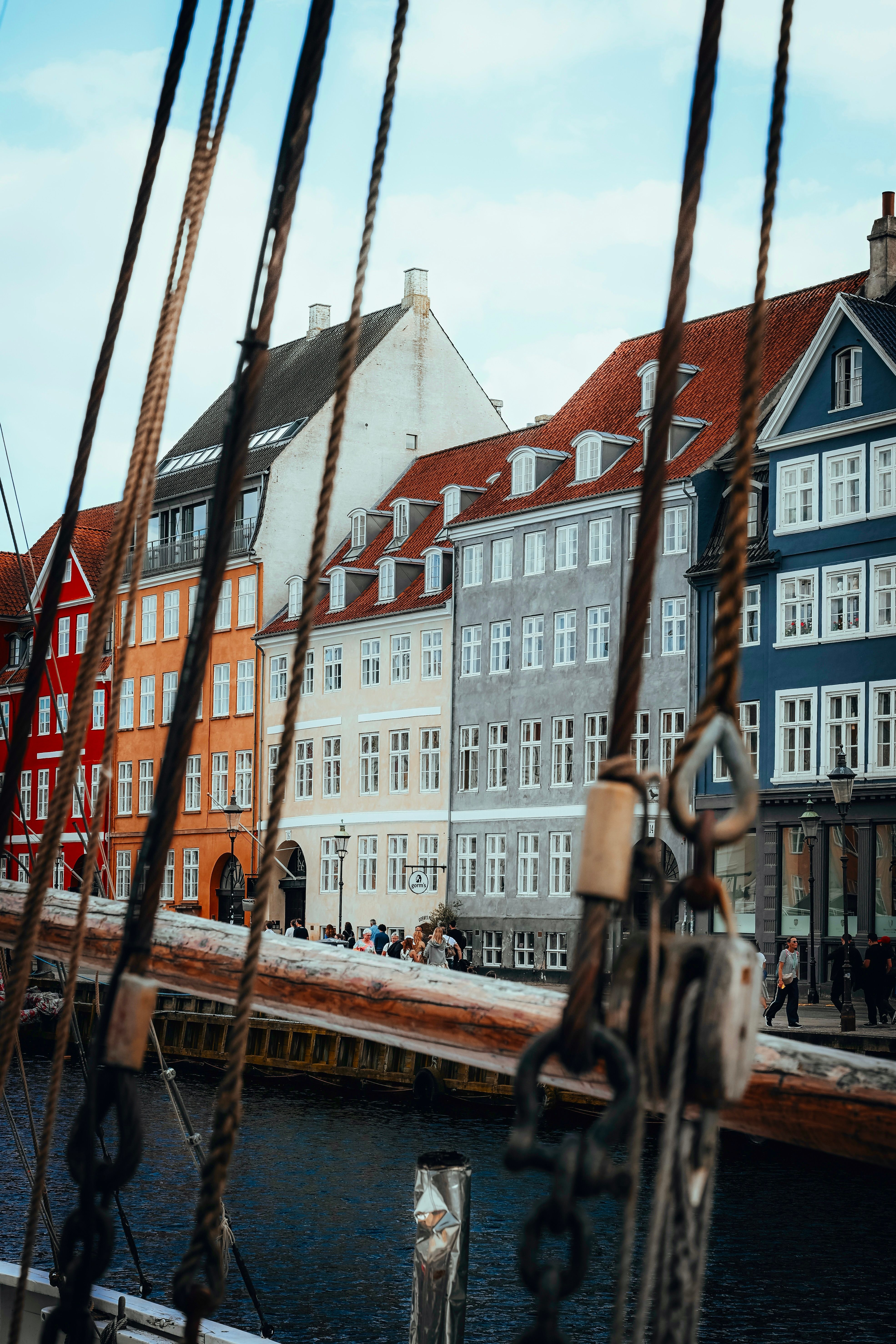 Scenic view of colorful buildings along Nyhavn waterfront in Copenhagen with sailing ropes in the foreground.