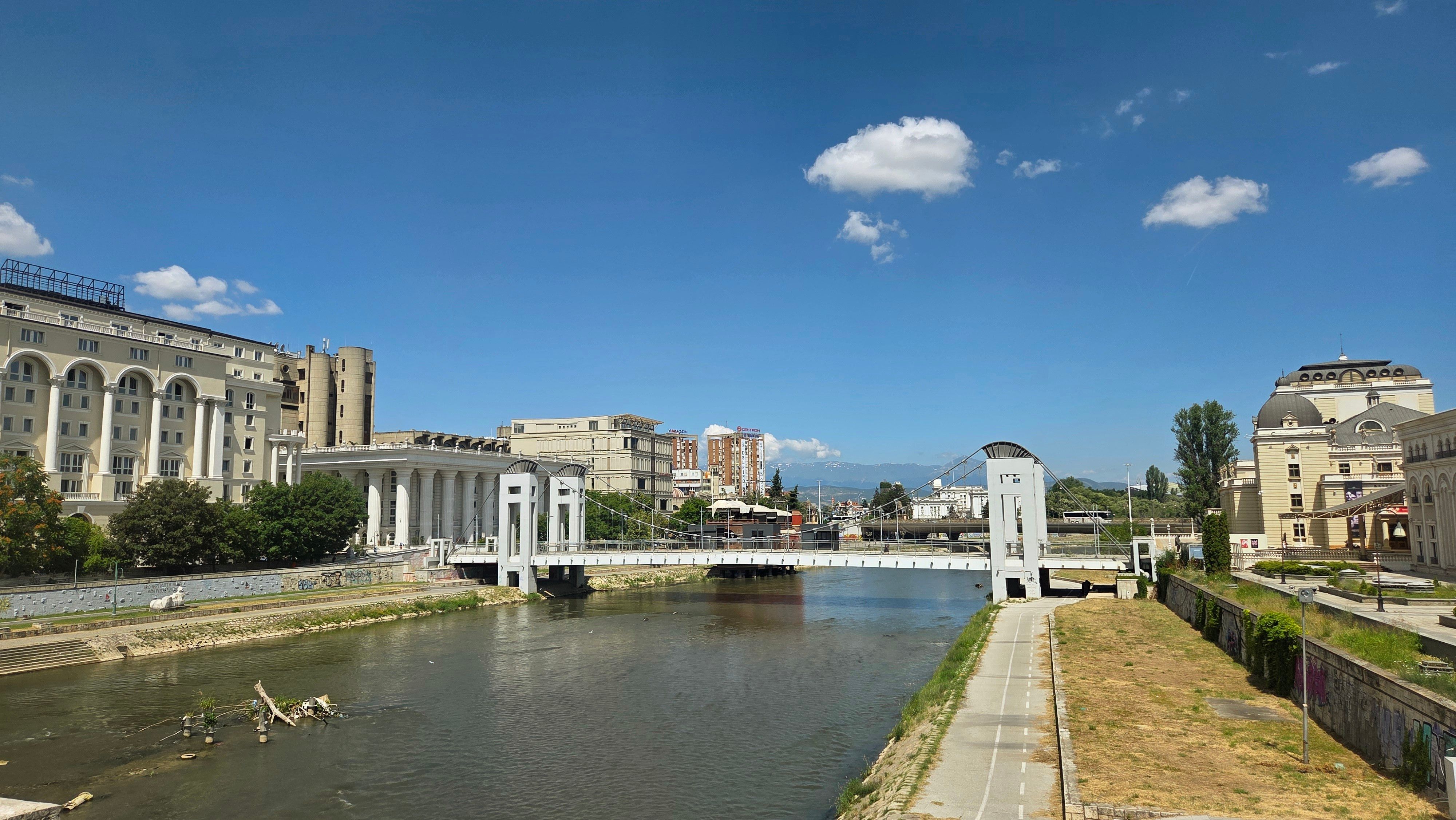 View of Skopje's architectural landmarks by Vardar River under a clear sky.